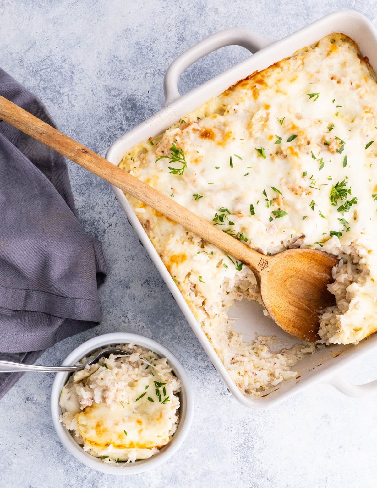 Casserole dish and a bowl full of cheesy tuna casserole, ready to eat.