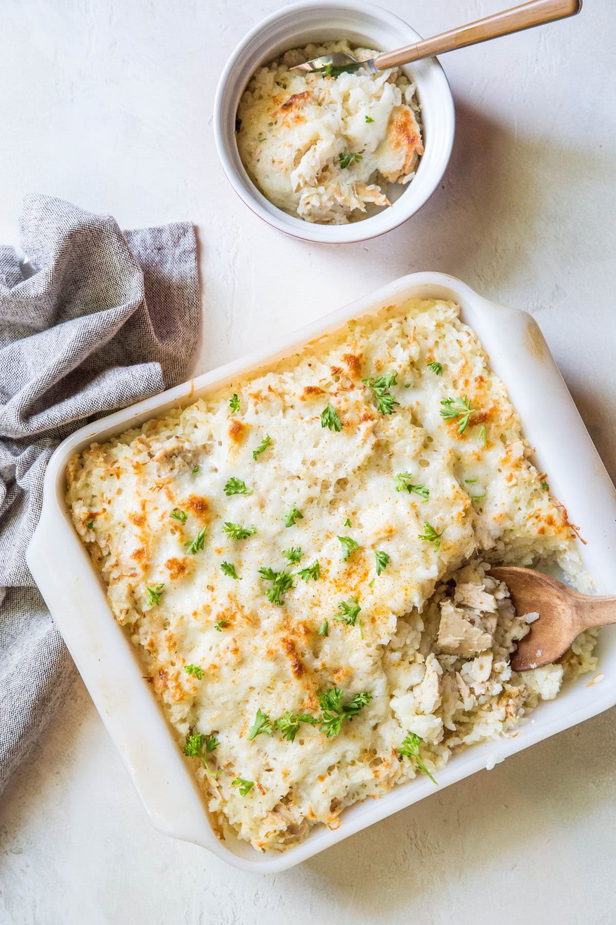 Large casserole dish full of tuna casserole fresh out of the oven with a small ramekin to the side full of a portion of casserole.