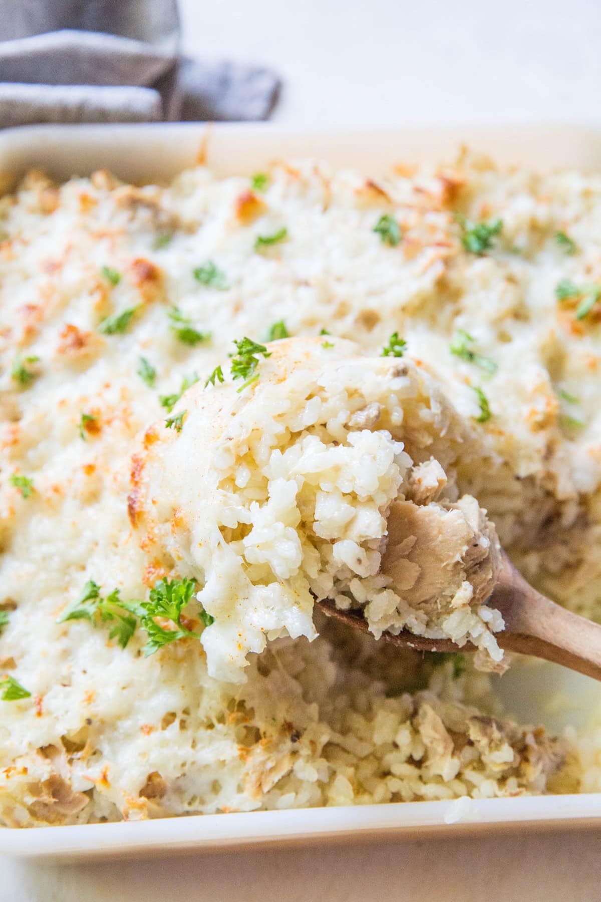 Large casserole dish with tuna rice casserole and a wooden spoon scooping some out.