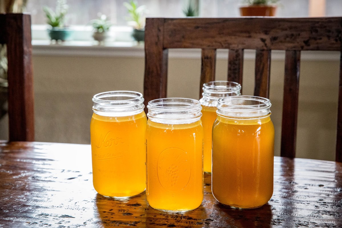 jars of bone broth sitting on a wooden table with a chair in the background.