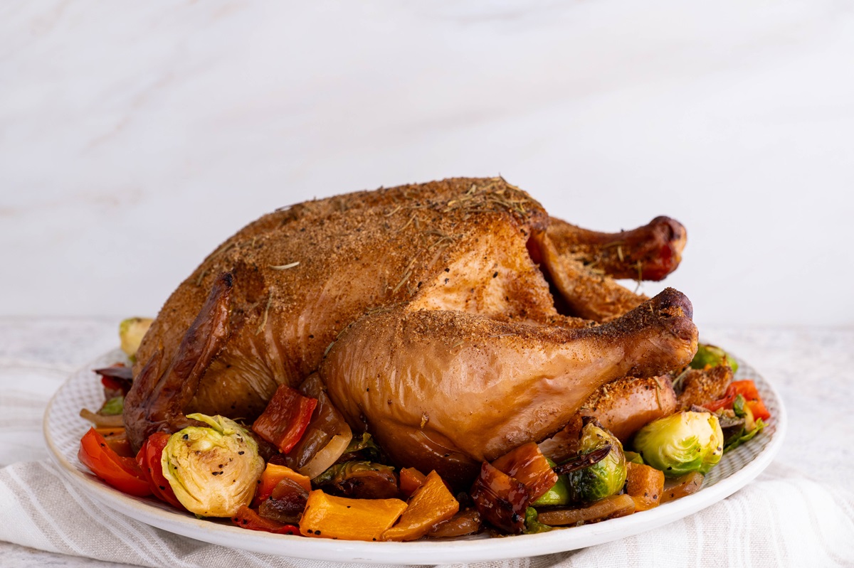 whole smoked chicken on a plate with roasted vegetables, ready to serve.