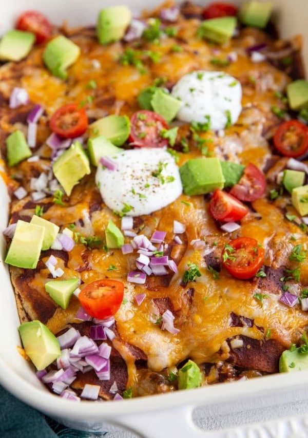 Big white casserole dish of beef enchiladas with corn tortillas.