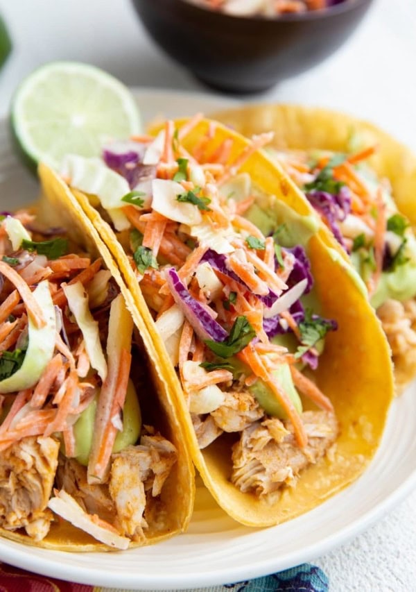 Three fish tacos on a plate with slaw and avocado sauce.