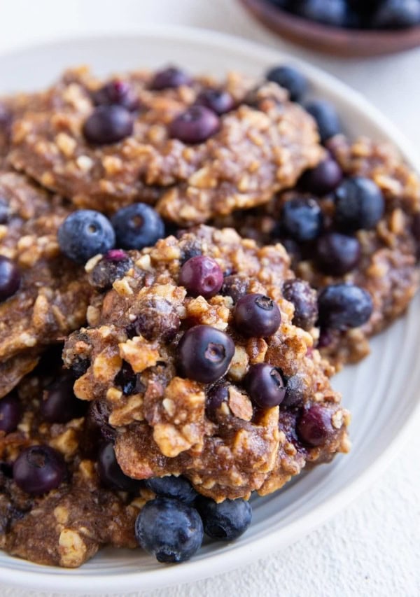 White plate of blueberry banana cookies with fresh blueberries all around.