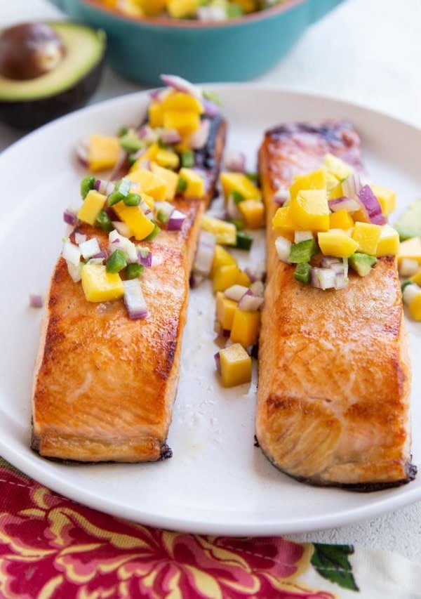 Two cooked salmon filets on a white plate with mango salsa on top.