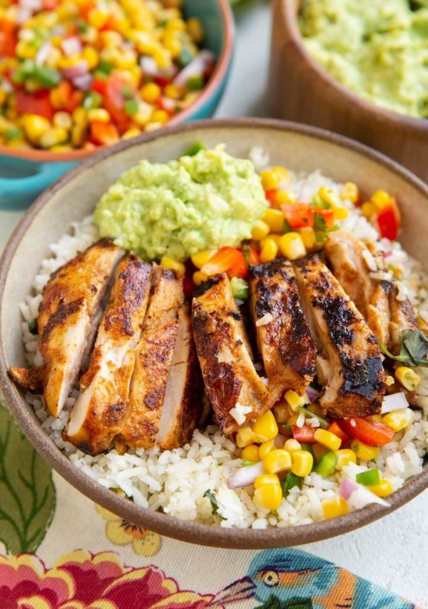 Chicken burrito bowl with corn salsa and guacamole in the background.