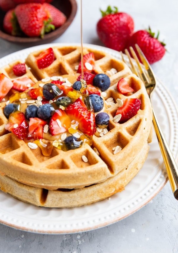 Honey being poured on top of waffles with fresh berries and almond butter.