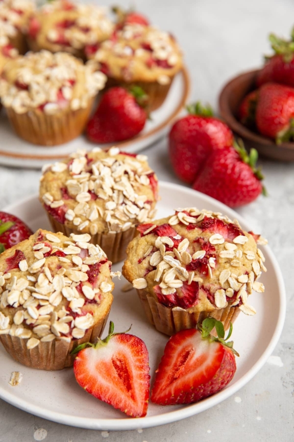 White plate of oatmeal strawberry muffins and fresh strawberries all around.