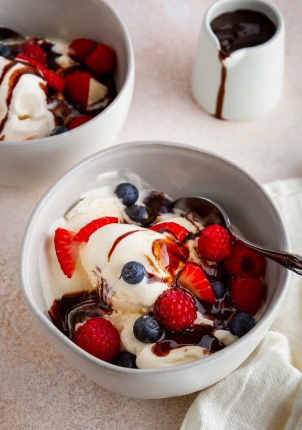 Two bowls of vanilla ice cream with fresh berries and chocolate sauce, ready to serve.