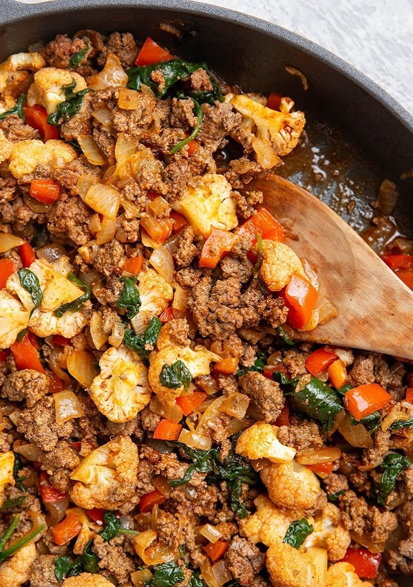 Skillet full of ground beef, cauliflower, bell peppers and spinach.