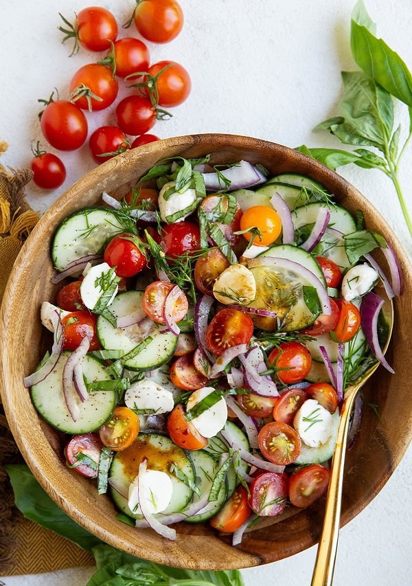 Wooden bowl of cucumber tomato salad with mozzarella cheese and fresh basil.