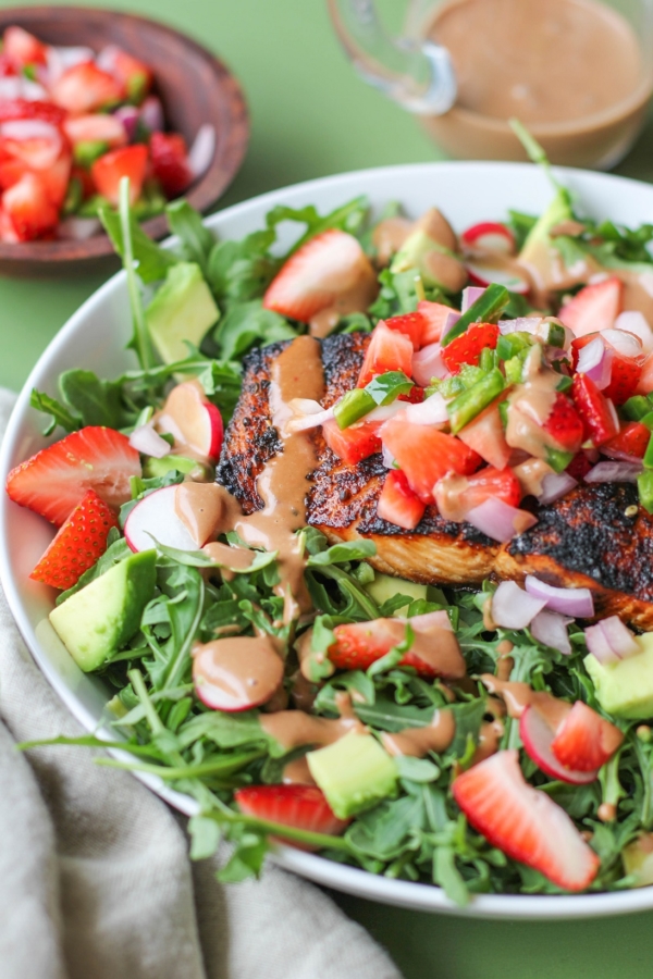 Grilled salmon in a bowl with salad ingredients, strawberry salsa and avocado on a green background.