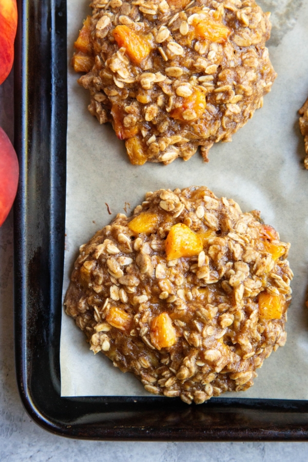 Peach oatmeal cookies on a baking sheet, fresh out of the oven with fresh peaches to the side.