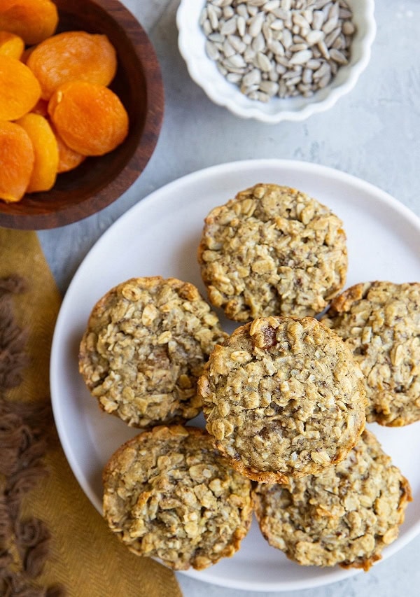 White plate of Aussie bites with bowls of dried apricots and sunflower seeds to the side.