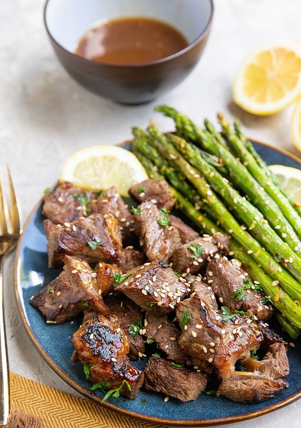 Steak bites on a blue plate with asparagus to the side.