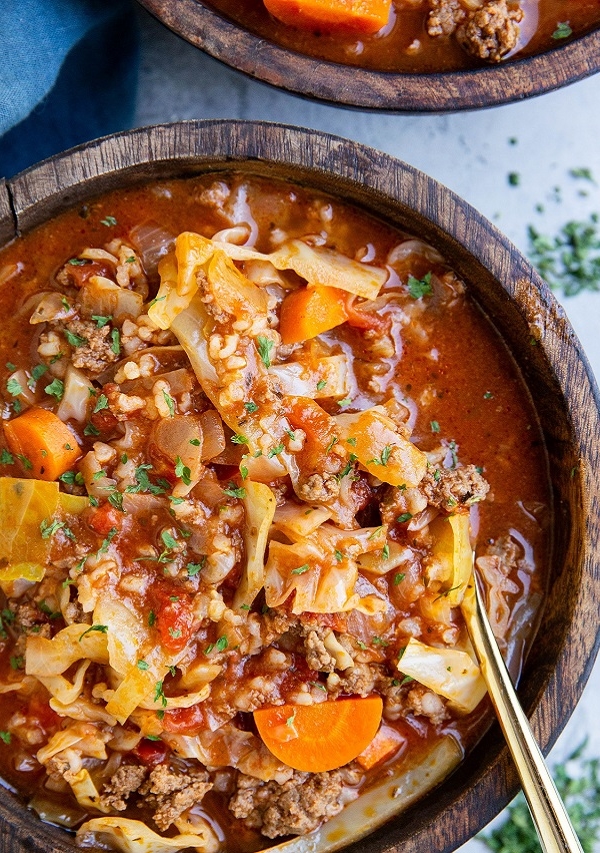 Two wooden bowls of cabbage roll soup with a golden fork, ready to eat.