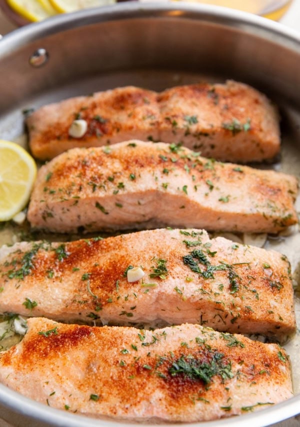 Four cooked salmon filers in a skillet, ready to serve.