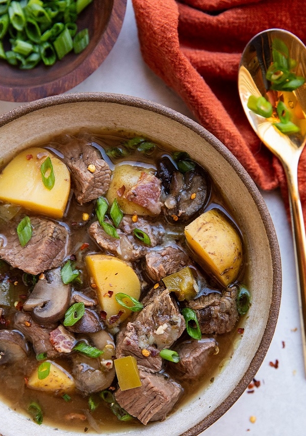 ceramic bowl of steak and potato soup sprinkled with green onions and red pepper flakes.