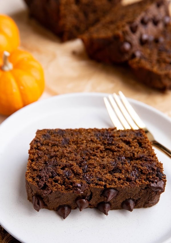 White plate with a thick slice of chocolate pumpkin bread and more slices in the background.