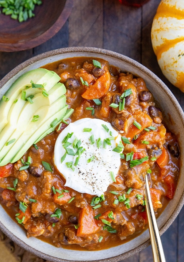 Bowl of pumpkin chili with black beans and avocado and Greek yogurt on top, ready to eat