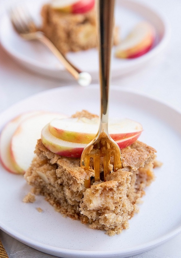 slice of apple cake on a plate with a gold fork taking a bite out of it.