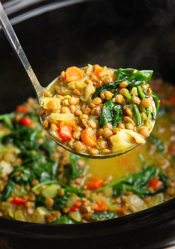 Crock pot of golden lentil soup with a ladle scooping out some soup.