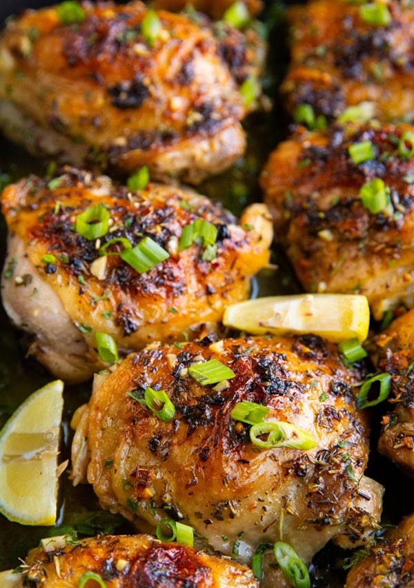 Crispy garlic butter baked chicken thighs in a casserole dish with green onions sprinkled on top and slices of lemon.