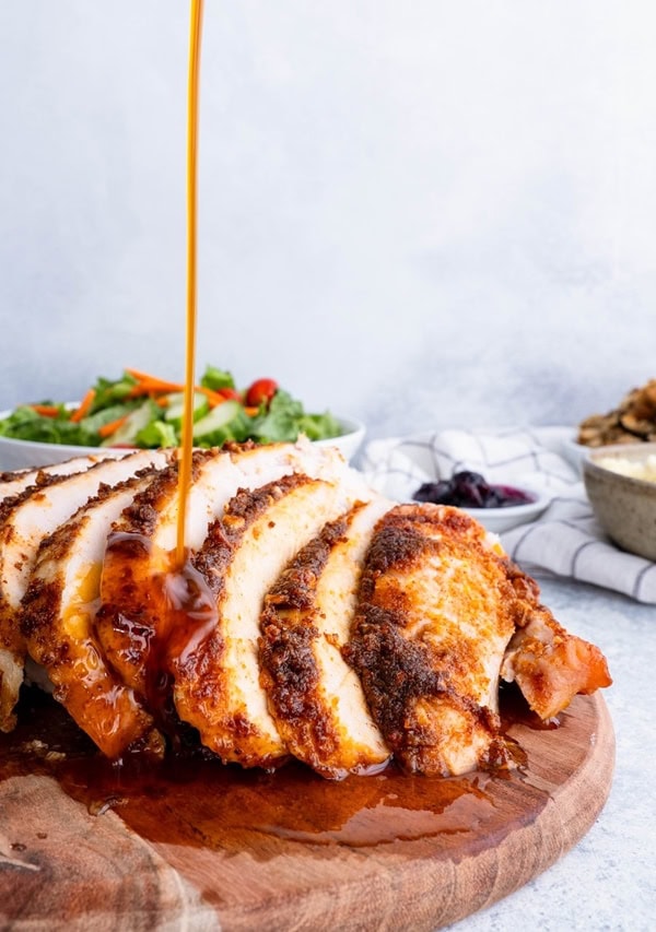 Sliced turkey breast on a cutting board being drizzled with gravy.