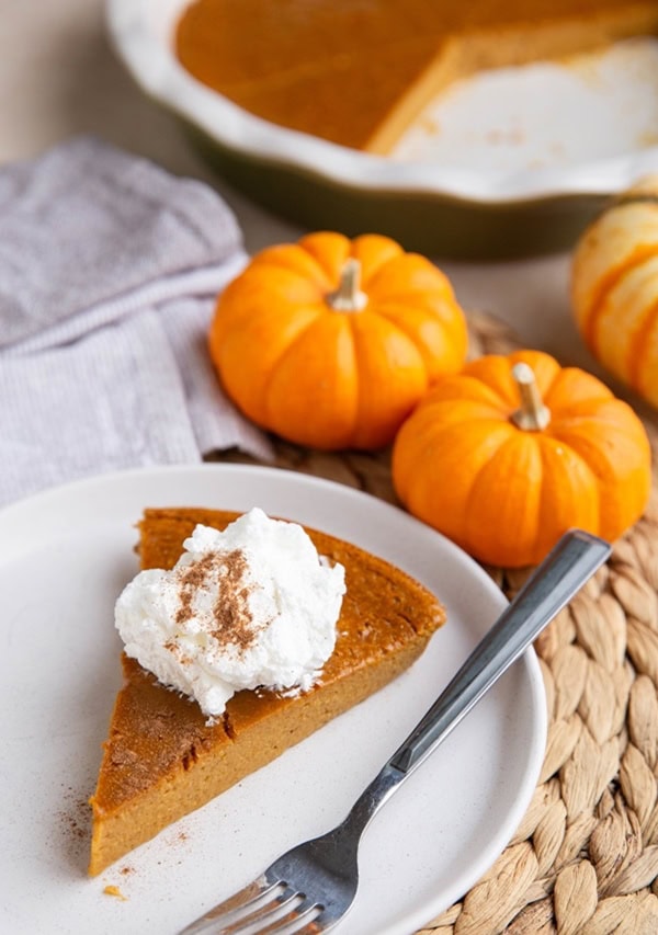 Slice of crustless pumpkin pie on a white plate with the rest of the pie in the background