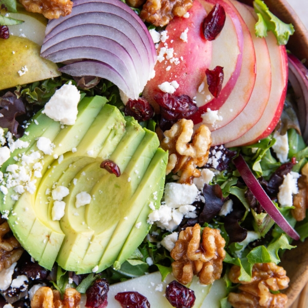 Wood bowl of salad with avocado, pears, apples, red onion, walnuts and feta cheese.