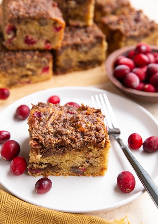 slice of cranberry orange cake on a white plate, with more slices of cake in the background.