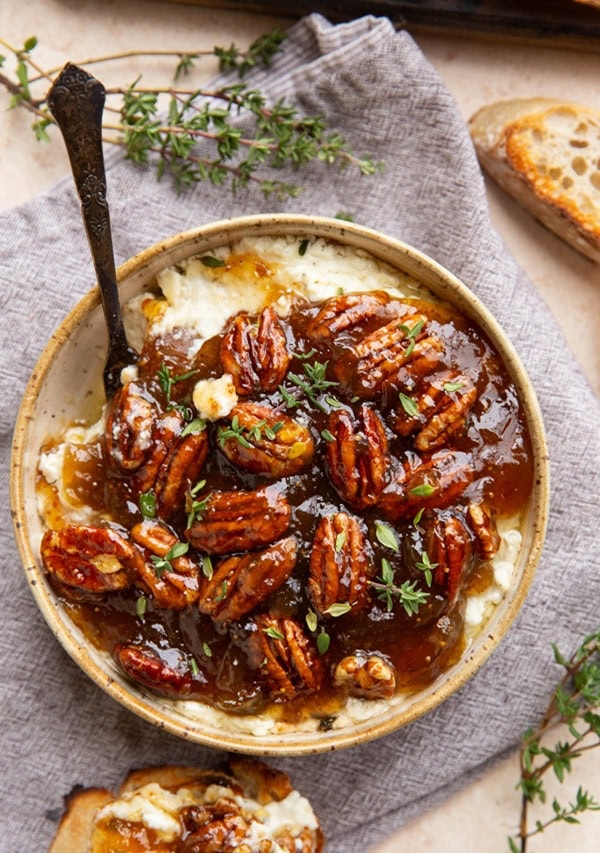 ceramic bowl of baked feta with fig jam and pecans.