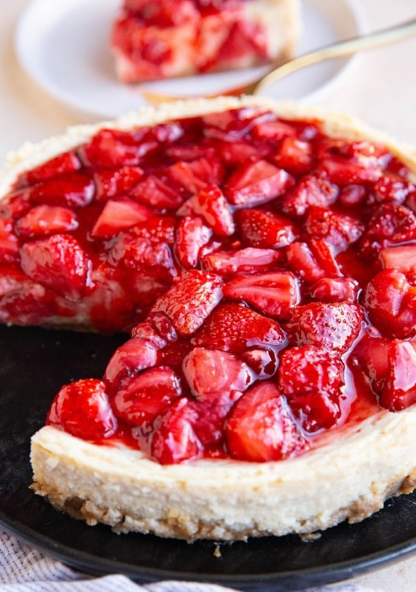 Cottage cheese cheesecake with strawberry compote on a black plate with a slice taken out and on a plate in the background.