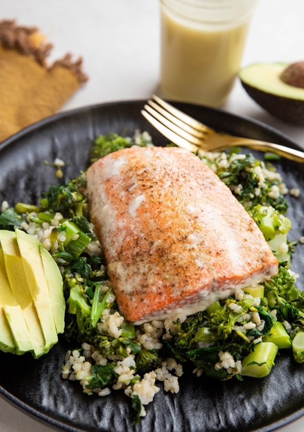 Baked sockeye salmon on a plate with rice, vegetables, and sliced avocado.