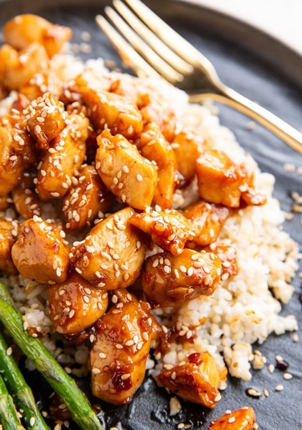 Sesame salmon on a black plate with steamed rice and asparagus, ready to eat.