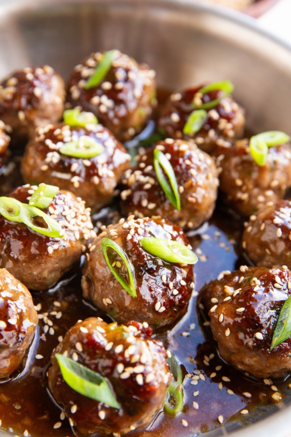 Stainless steel skillet full of glazed meatballs with green onions and sesame seeds on top.