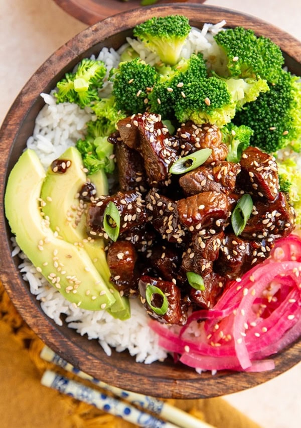 Wooden bowl of rice, steak, broccoli, and pickled red onions.