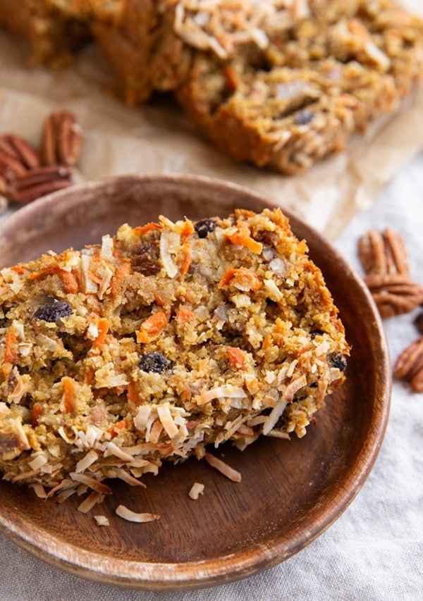 Thick slice of carrot cake bread on a wooden plate with the loaf in the background.