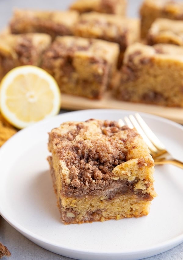 Slice of lemon coffee cake on a white plate with the rest of the slices of coffee cake in the background.