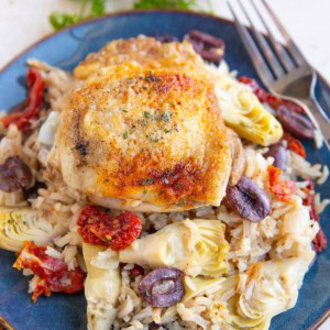 Blue plate of chicken and rice with artichoke hearts, olives, and tomatoes, ready to serve.