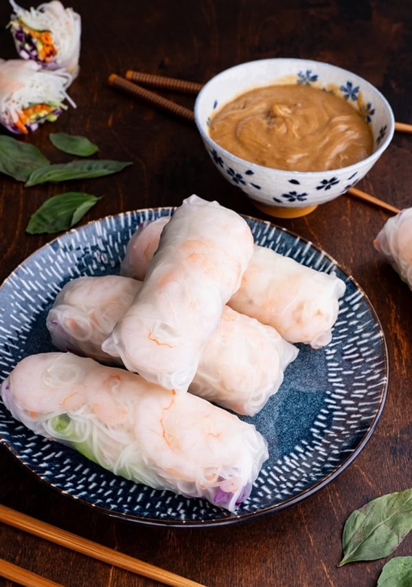 Plate of shrimp spring rolls with bowl of peanut sauce in the background.