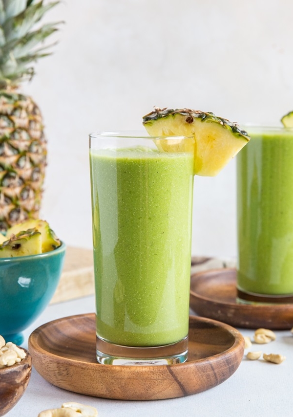 Two green smoothies in glasses with fresh pineapple garnishing the glass
