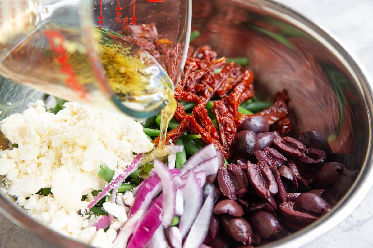 Pouring salad dressing into the mixing bowl with the salad ingredients.