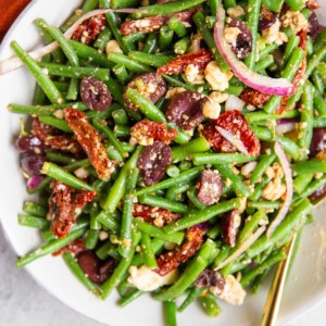 Mediterranean Green Bean salad in a white bowl with a golden spoon and a red napkin, ready to serve.