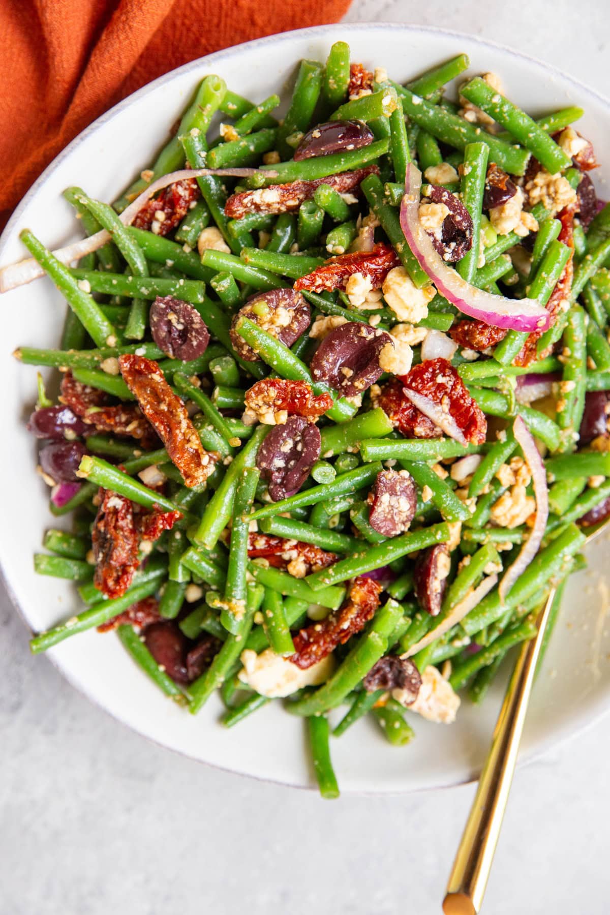 Mediterranean Green Bean salad in a white bowl with a golden spoon and a red napkin, ready to serve.