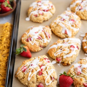 Baking sheet of almond flour strawberry scones with fresh strawberries and a napkin to the side.