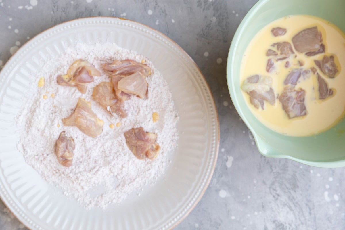 Dredging chicken in egg mixture then in the flour mixture in a bowl and on a plate to make bang bang chicken.