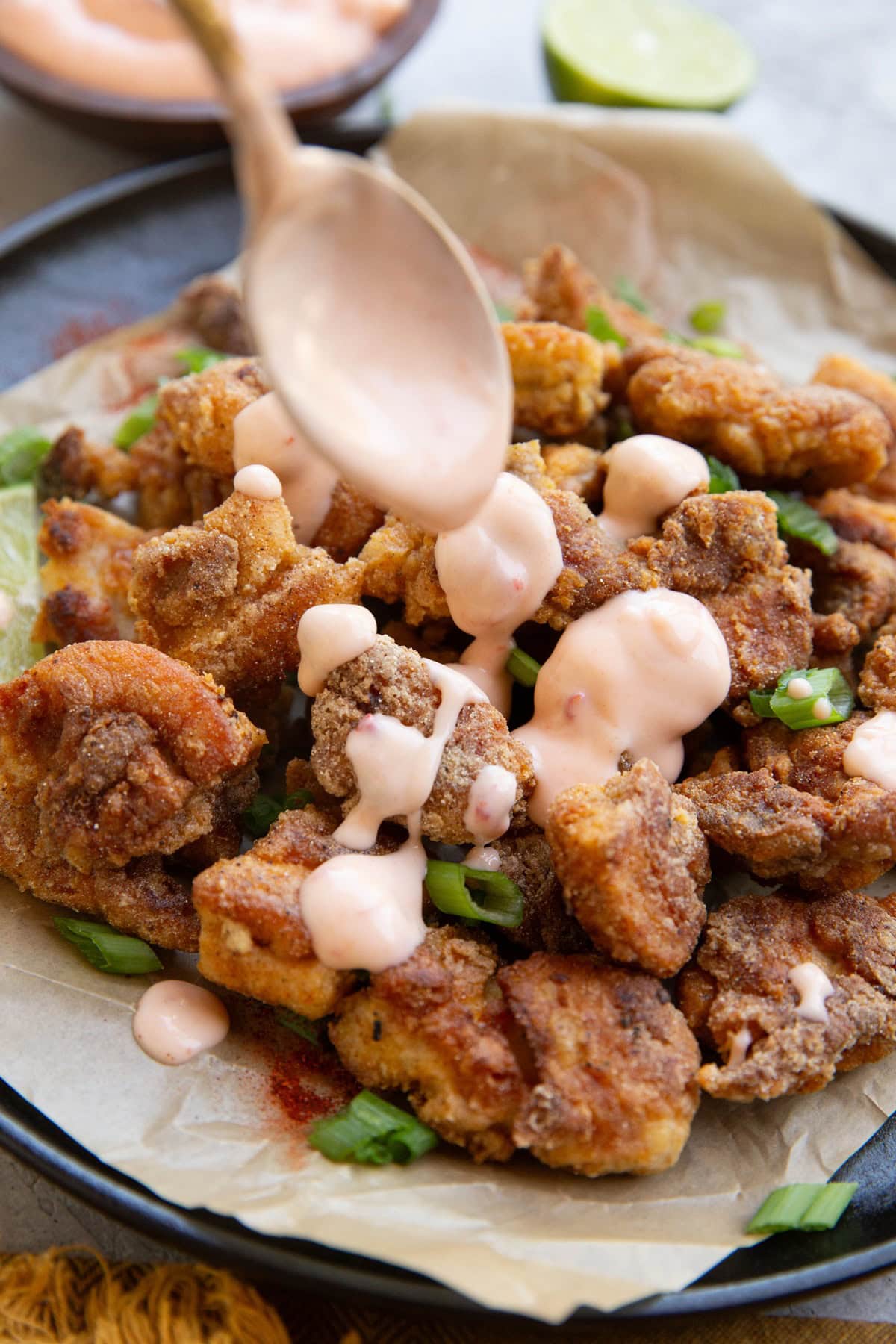 Drizzling bang bang sauce over crispy chicken using a spoon.