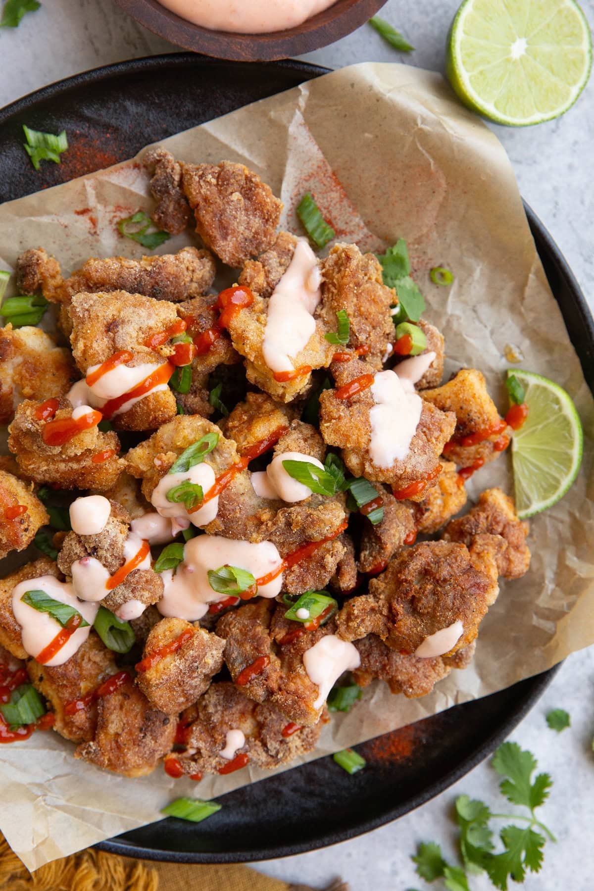 Plate of crispy bang bang chicken drizzled with sauces with fresh lime and cilantro to the side, ready to serve.