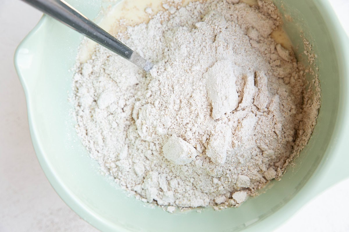 Mixing bowl with wet ingredients in the bottom and dry ingredients on top to be mixed together for muffin batter.